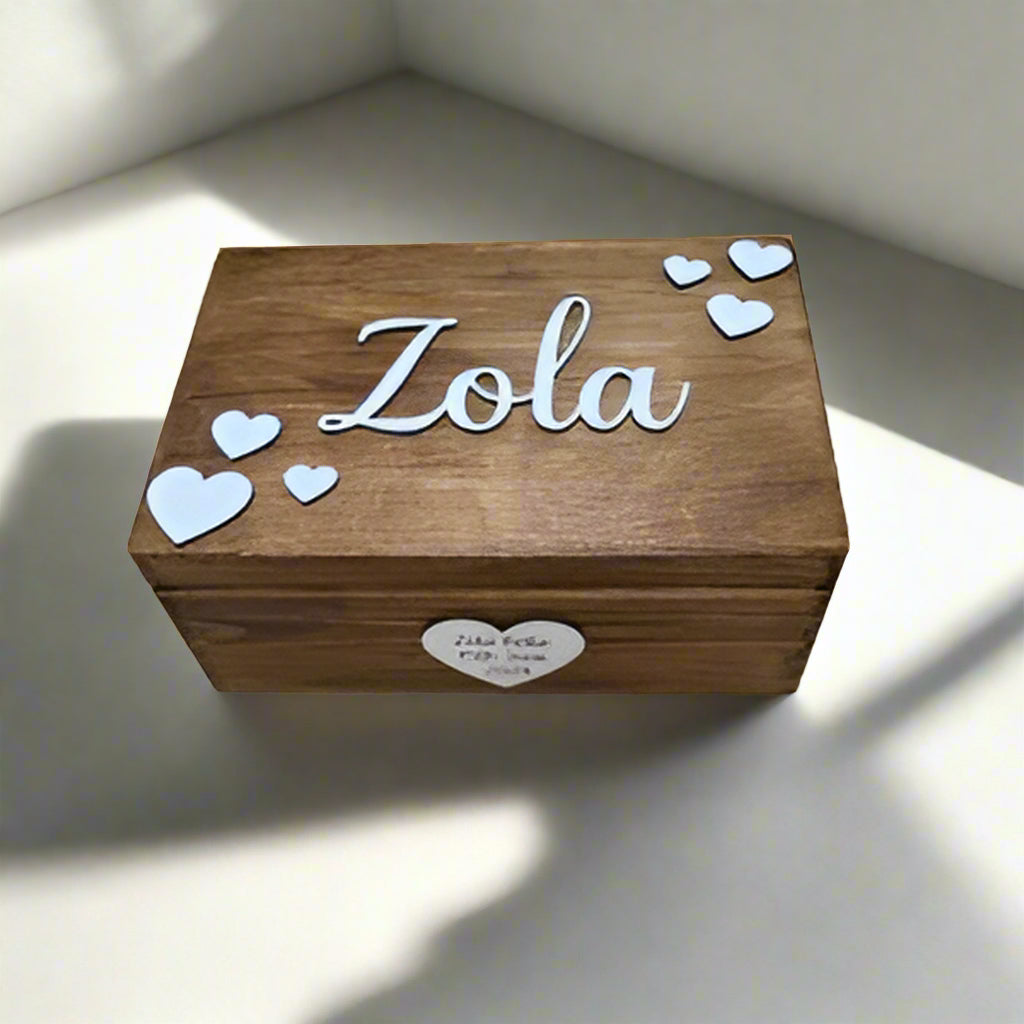 Wooden box with 'Zola' engraved on it, surrounded by heart-shaped decorations on a wooden surface.