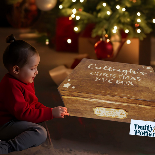 Child opening a wooden Christmas Eve box in front of a decorated Christmas tree.