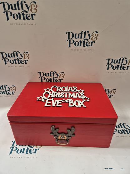 A red wooden Christmas Eve box with 'CROIAS CHRISTMAS EVE BOX' in white lettering on the lid, featuring a small reindeer antler clasp with a pink nose. The box is photographed against a white background printed with the 'Duffy & Porter' brand logo.