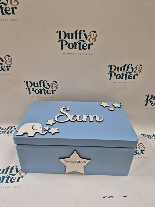 A personalized light blue wooden keepsake box with laser-cut white details, including the name 'Sam', stars, a small elephant, and a star with the date '12.05.