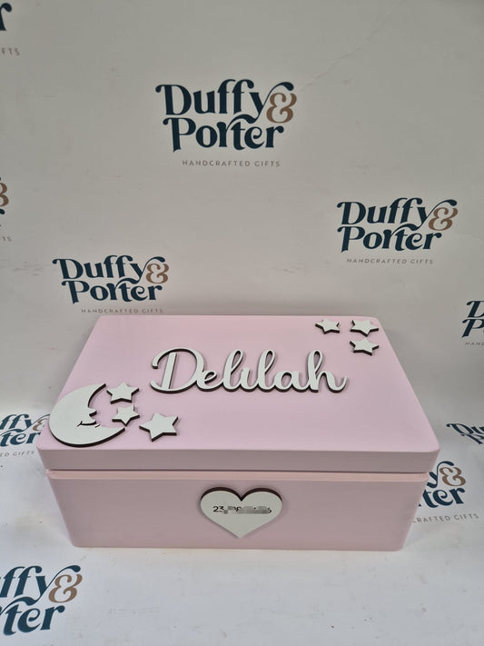 A pink wooden personalised keepsake box with whitelettering that reads 'Delilah' and silver crescent moon and star decorations on the lid, plus a heart-shape on the front. The box is photographed against a white background with repeated 'Duffy & Porter' logos visible.