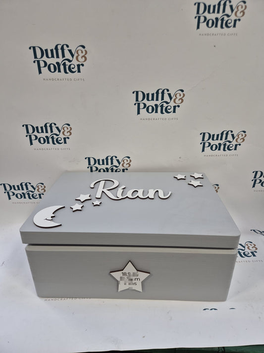 A light gray wooden keepsake box with silver-colored cutout decorations, including a crescent moon, stars, and the name 'Rian' on the lid, set against a white background with a repeating 'Duffy & Potter' watermark pattern.