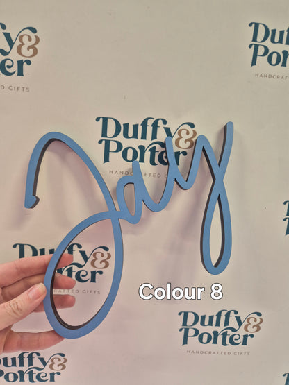 A hand holds a light blue 3D decorative script wall sign spelling 'Jay' against a white background with repeated 'Duffy & Porter' logos and a text overlay reading 'Colour 8'.